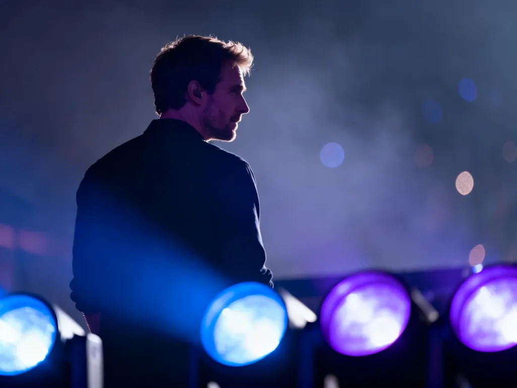 Dawid Podsiadło na scenie podczas koncertu, oświetlony nastrojowym niebiesko-fioletowym światłem.