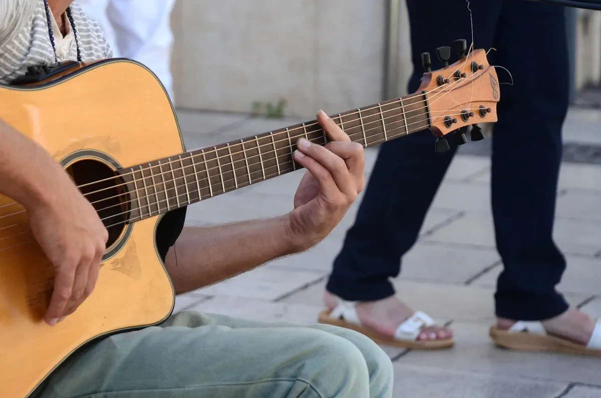 Dłoń gitarzysty wykonująca chwyt barowy na gryfie gitary.